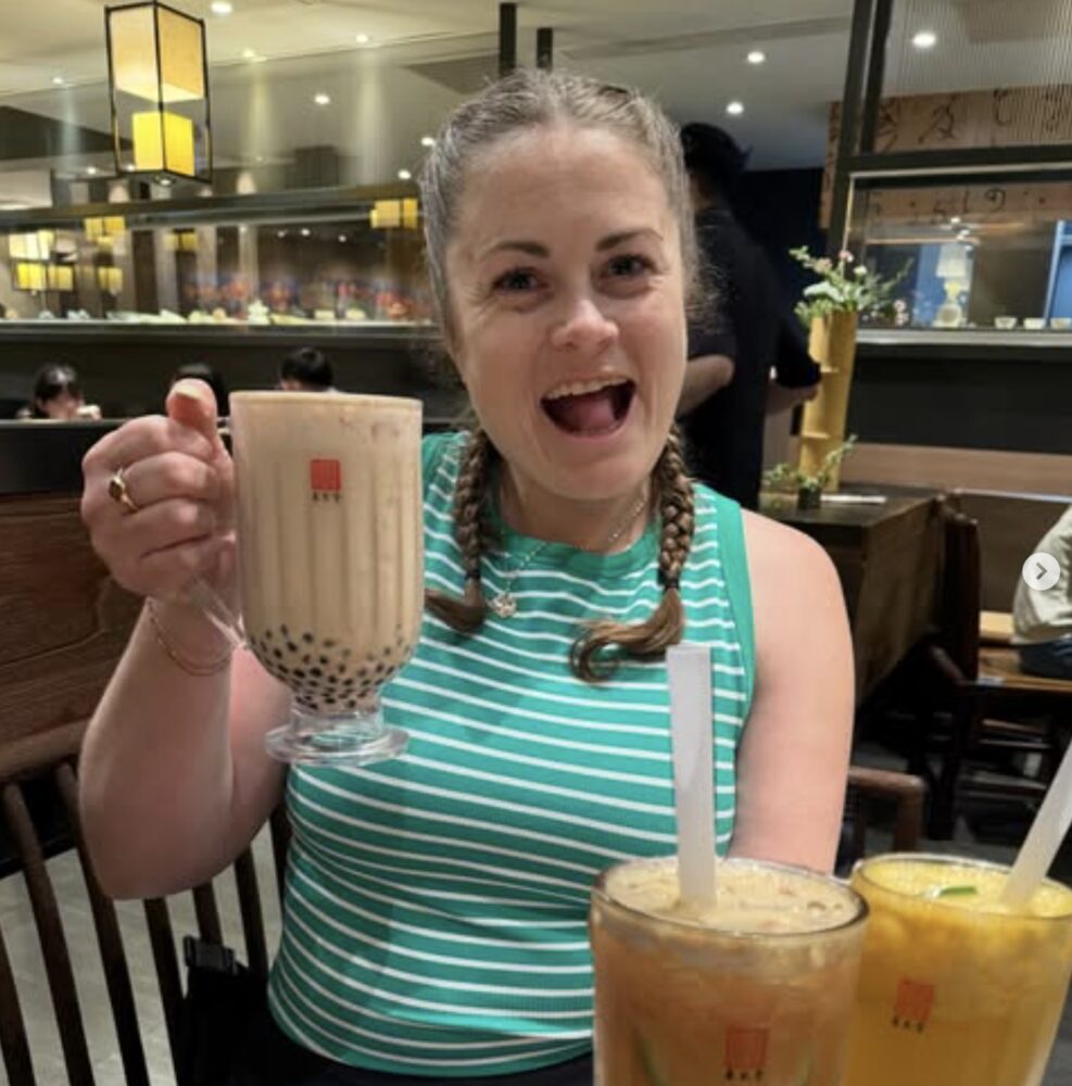 Leah with braids, grinning wide and holding up a giant bubble tea